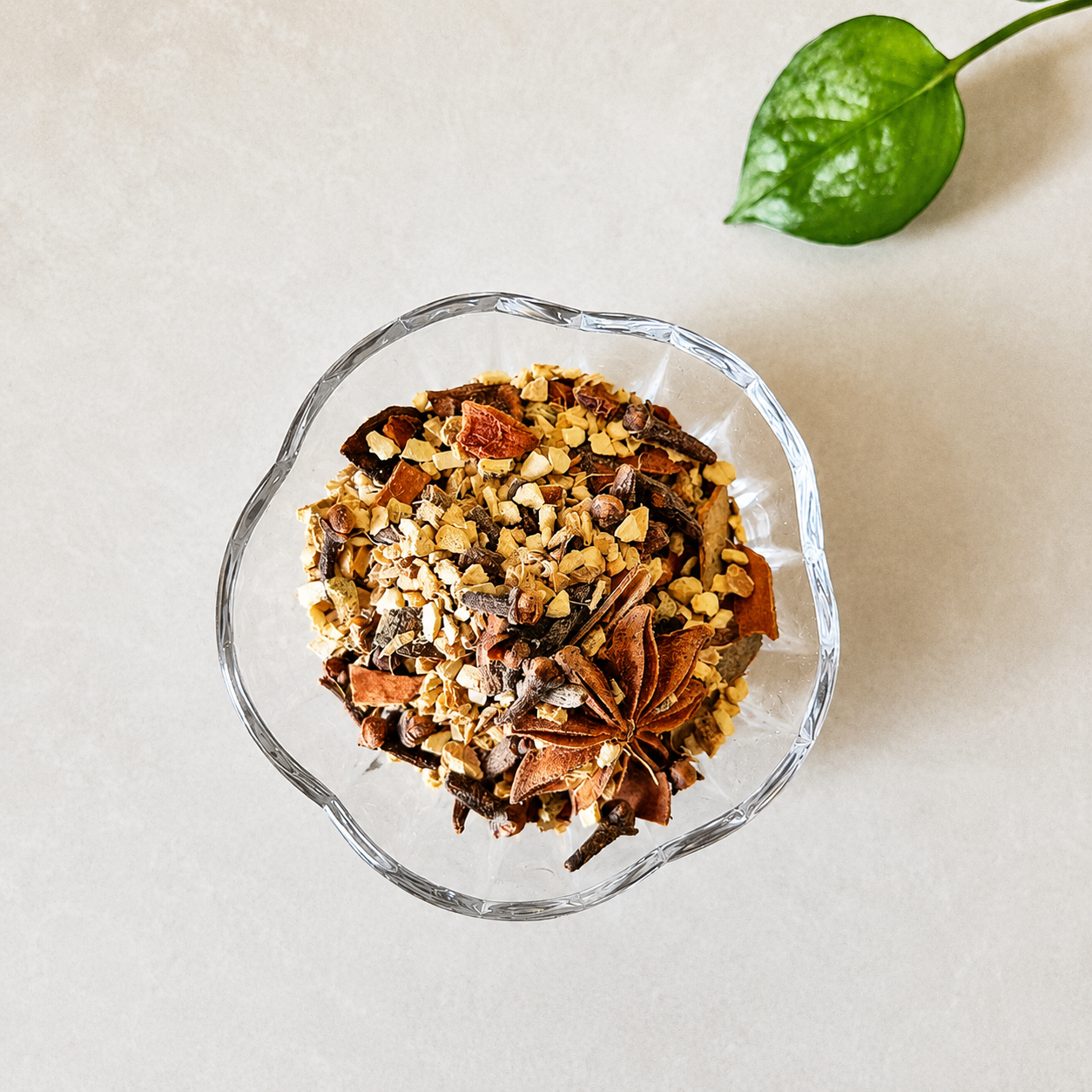 Daily Defense herbal spice blend with ginger, cinnamon, clove and dried orange peel in a clear glass bowl on a light background with green leaf accent.
